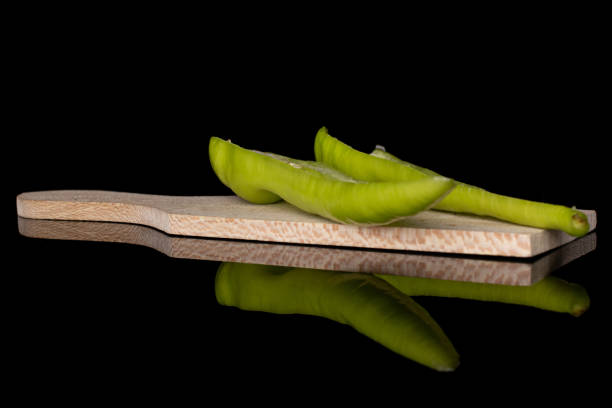 Group of two halves of hot green pepper banana on wooden cutting board isolated on black glass