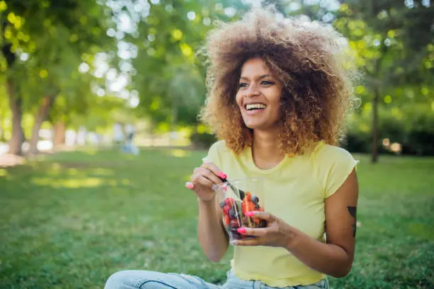 Photo of Beautiful girl resting on the grass and eating fruit salad