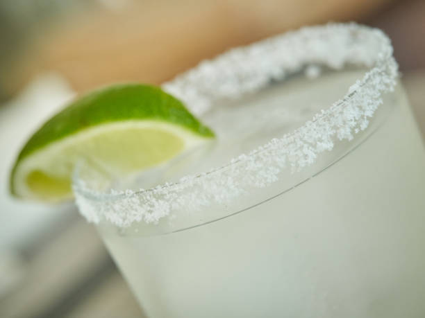 Glass rim garnished with salt and slice of lime , margarita drink light green , shallow depth of field stock photo