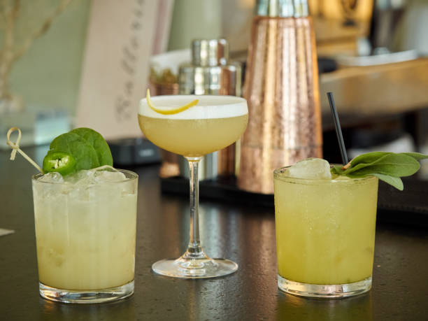 Three yellow colored cocktail drinks on a bar counter, copper shakers on a background stock photo