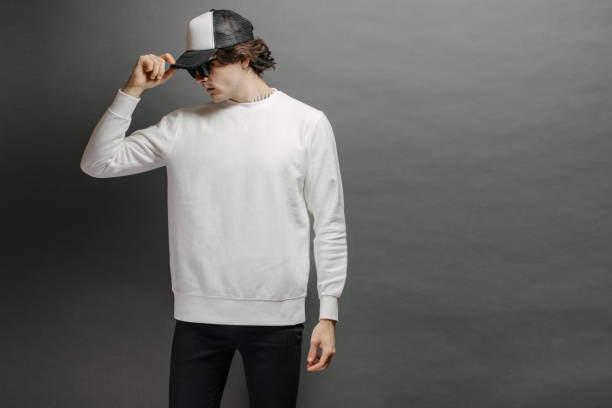 istock Man wearing blank white sweatshirt and empty baseball cap standing over gray background. Sweatshirt or hoodie for mock up, logo designs or design print with free space. 1191691308