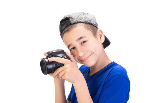 Portrait of happy teenage boy holding a digital photo camera and looking at camera with content smile against white background. Horizontal composition. Studio shot.