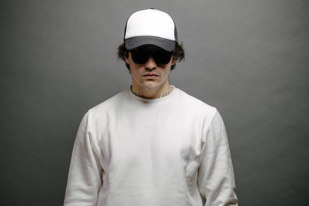 istock Man wearing blank white sweatshirt and empty baseball cap standing over gray background. Sweatshirt or hoodie for mock up, logo designs or design print with free space. 1191694100