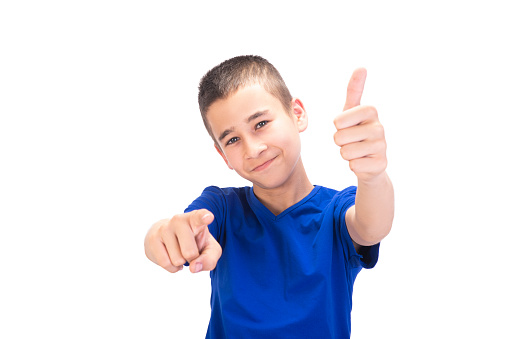 Portrait of smiling teenage boy gesturing thumbs up while he pointing at camera over white background. Horizontal composition, studio shot.