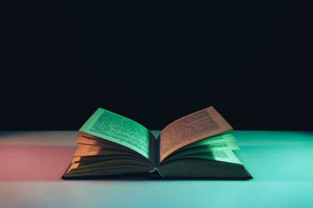 istock Beautiful open old book in the color light on a table and night background. 1191695336