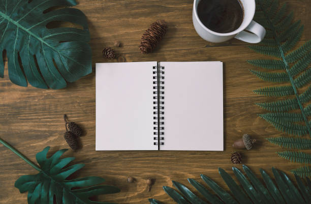 Background top view of notebook, cup of coffee, green leaves pine cones on wood table background. Copy space of creative flat layout top view, business desk minimal nature style concept. vista superior de fondo de cuaderno, taza de café, hojas verdes conos de pino sobre fondo de mesa de madera. copie el espacio de la vista superior de diseño plano creativo, el concepto de estilo mínimo de la naturaleza del escritorio de negocios.