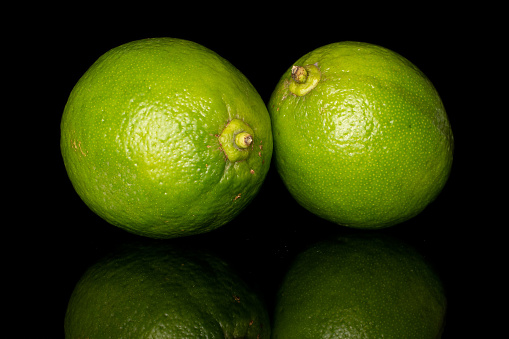 Group of two whole sour green lime isolated on black glass