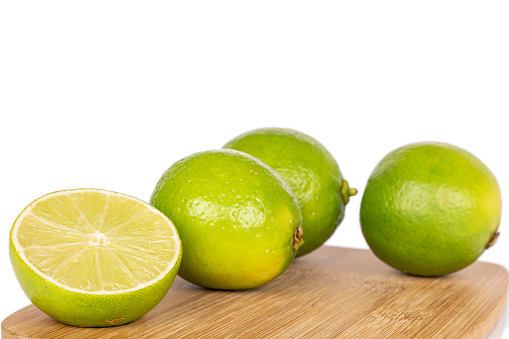 Group of three whole one half of sour green lime on bamboo cutting board isolated on white background