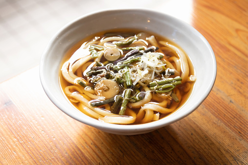 Japanese udon noodles with soup in a bowl on table with sunlight through the window.
