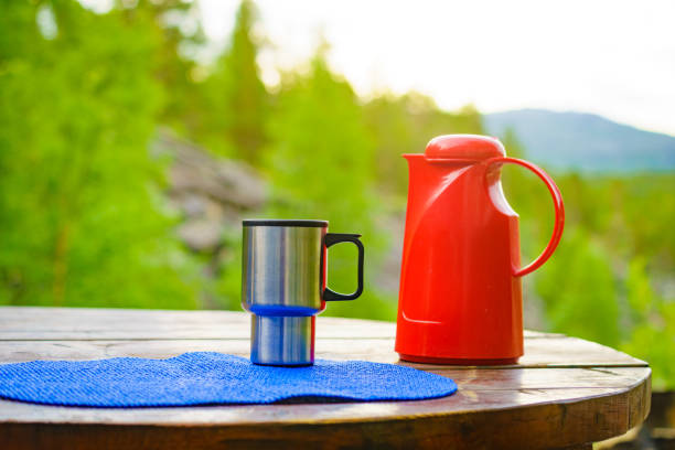 Picnic site table with thermos and thermal mug, norwegian mountains nature in the background. Camping with thermos.