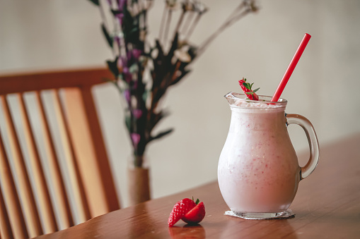 Glass of fresh strawberry milkshake, smoothie and fresh strawberries on wooden table. Healthy and sweet drink concept.