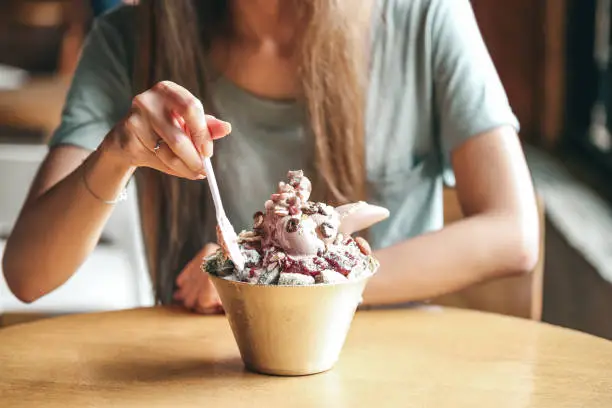 Female young lady eat Korean Bingsu ice with chocolate icecream. with ricecake and nuts. selective focus on bingsu blur people.