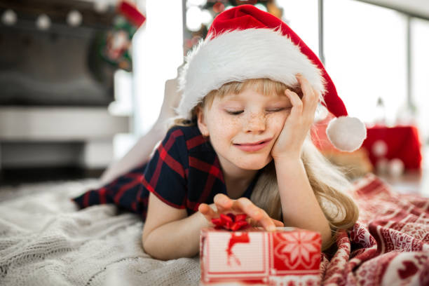 istock Happy girl in santa hat lying on floor with red present 1191707413