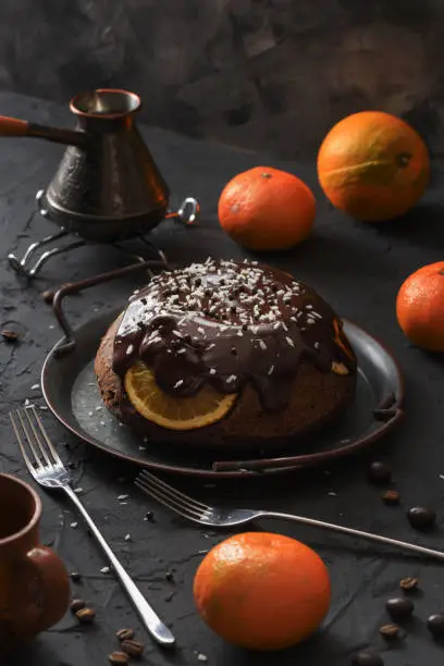 Homemade winter dessert. Traditional British steam chocolate pudding with oranges and clementines on vintage dish with coffee on black background low key