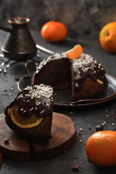 Traditional British steam chocolate pudding with oranges, clementines and coconut shreds served with coffee on wood slab on black background low key