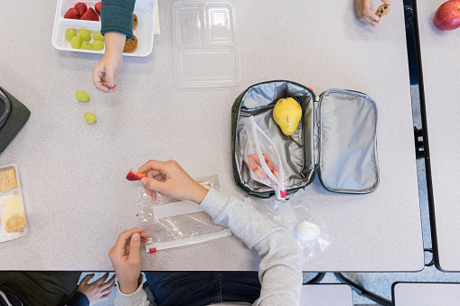 Unrecognizable schoolchildren eat a healthy lunch in the school cafeteria.