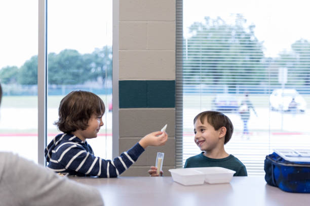 Schoolboys trade food during lunchtime Male elementary students trade food during lunch in the school cafeteria. food elementary student healthy eating schoolboy stock pictures, royalty-free photos & images