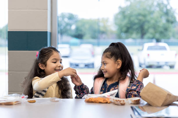 Twin sisters share lunch in the school cafeteria The two young twin sisters share lunch with each other in the elementary school cafeteria. school lunch child food lunch stock pictures, royalty-free photos & images