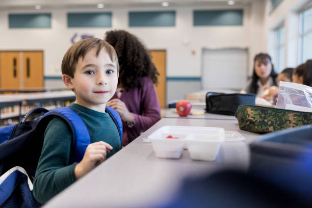 Nervous elementary school boy sits at cafeteria table The cute elementary school boy is nervous on his first day in the school cafeteria. food elementary student healthy eating schoolboy stock pictures, royalty-free photos & images