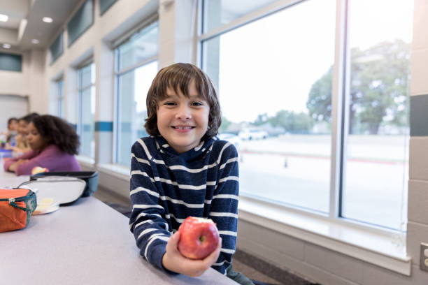 istock Young boy smiles for camera while eating apple in cafeteria 1191725467