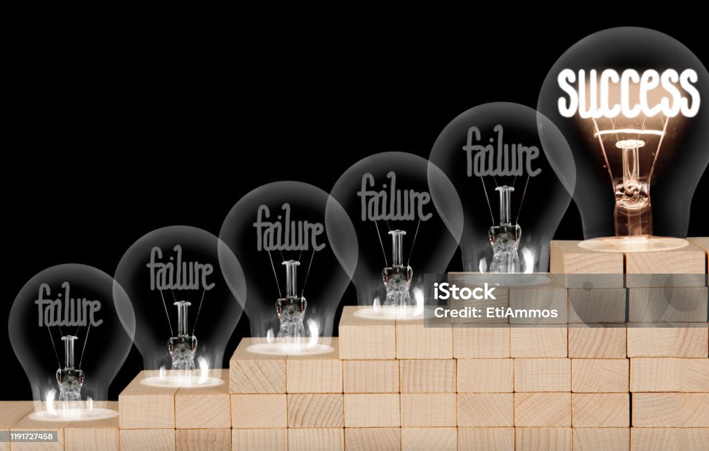 Light Bulbs with Failure and Success Concept Group of shining and dimmed light bulbs on wooden block ladder with fibers in a shape of Failure and Success concept words isolated on black background. Failure Stock Photo