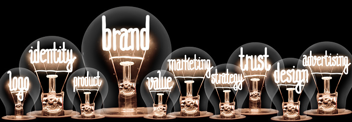 Group of light bulbs with shining fibers in a shape of Brand, Identity, Value, Marketing and Trust concept related words isolated on black background; horizontal composition