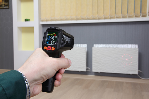 Infrared thermometer in hand measures the temperature of heating radiators in a room