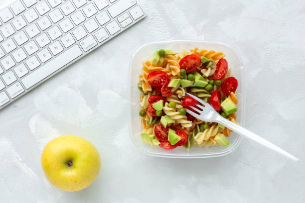 Italian pasta with vegetables on office desk with keyboard