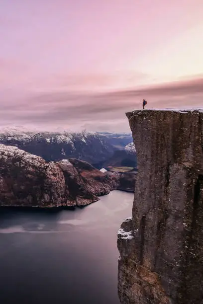 Photo of Man hiker standing on the famous Preikestolen over the Lysefjord, beautiful colors at sunset, Ryfylke, Rogaland, Norway