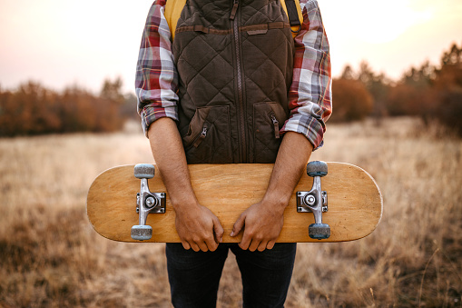 Male hiker carrying skateboard on grass field