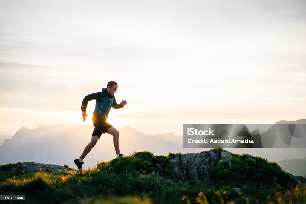 Young man runs on mountain ridge at sunrise He leaps into the morning air Running Stock Photo