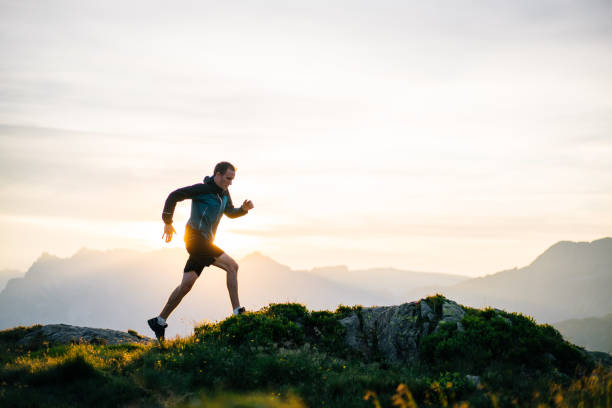 Young man runs on mountain ridge at sunrise stock photo