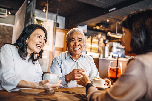 Group of three Asian senior friends sitting and talking in cafe, laughing and having fun