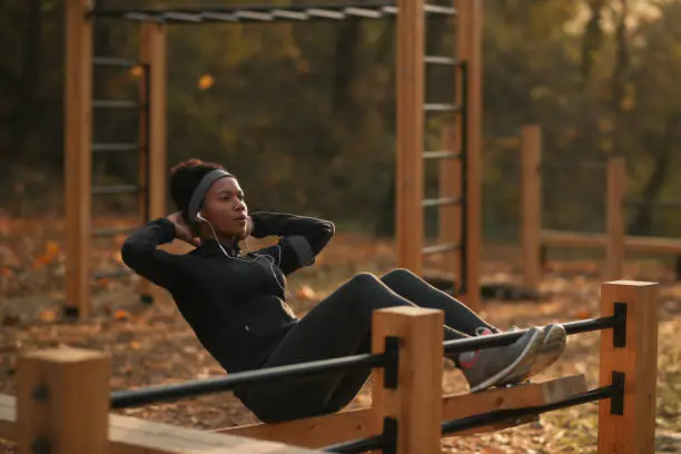 Black sportswoman exercising sit-ups while being at outdoor gym at the park.