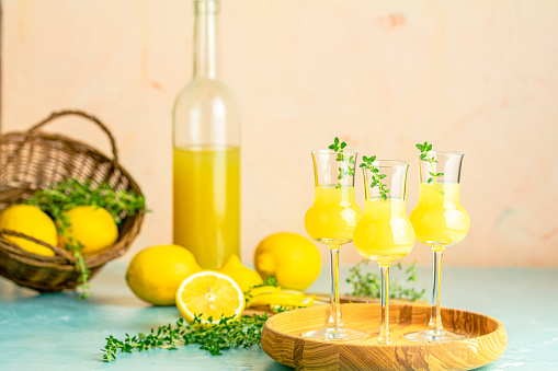 Limoncello with thyme in grappas wineglass with water drops on light concrete table. Artistic still life on light background with sunny light.