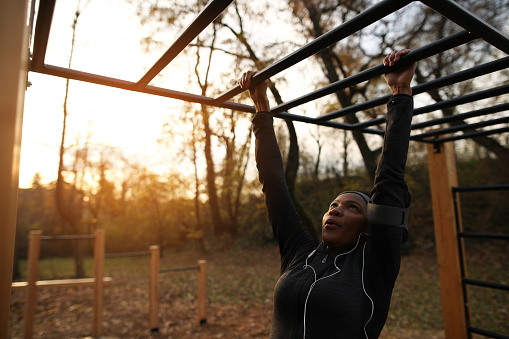 African American sportswoman crossing over horizontal bars at outdoor gym in the park.