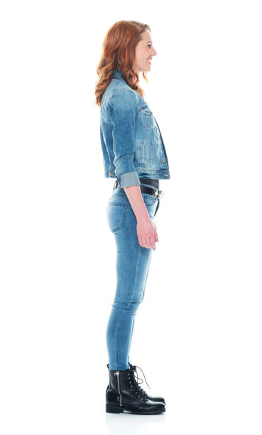 full length / side view / profile view / one person of 20-29 years old adult beautiful redhead / long hair caucasian female / young women standing wearing double denim / jeans / pants / denim jacket / boot / rolled-up sleeves / jacket / warm clothing - one young woman only only young women one woman only 20 25 years imagens e fotografias de stock