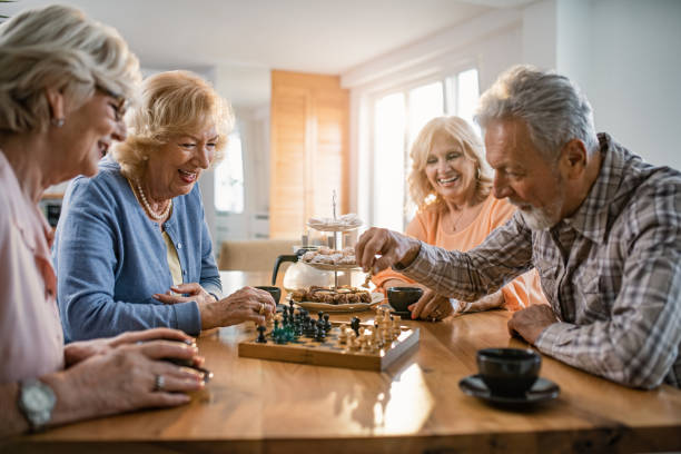 Happy seniors relaxing at home and playing chess. Happy mature friends playing chess while relaxing at home. Focus is on woman in blue sweater. senior chess stock pictures, royalty-free photos & images