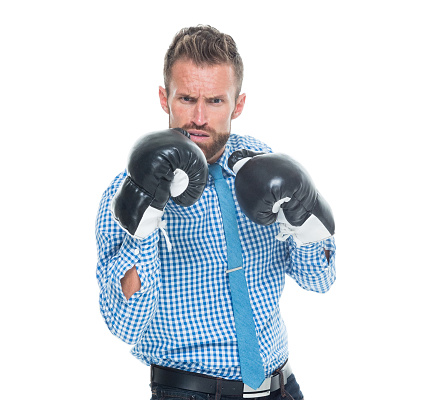 One man only / one person / waist up / front view / looking at camera of 30-39 years old handsome people brown hair / with beard / short hair caucasian male / young men business person / businessman standing wearing smart casual / blazer - jacket / gingham / necktie / jeans / pants / boxing glove / glove who is angry / frustration / displeased / aggression / despair / struggle / serious and showing fist who is in fighting stance / fighting / punching