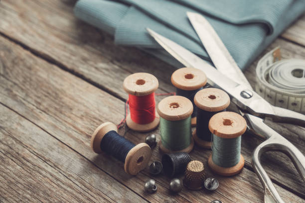 istock Retro sewing items: tailoring scissors, thimbles, buttons, wooden thread spools, measuring tape and green fabric. 1191765406