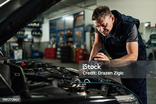 istock Auto mechanic using lap while examining car engine in repair shop. 1191773907