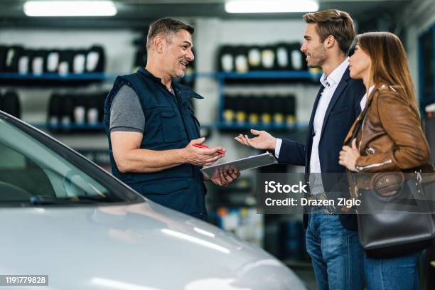 Junge Glücklich Paar Im Gespräch Mit Automechaniker In Autowerkstatt Stockfoto und mehr Bilder von Autowerkstatt