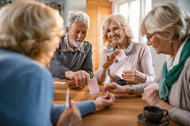 Small group of mature friends enjoying while playing cards at home. Happy seniors having fun while playing card game at home. poker card game stock pictures, royalty-free photos & images