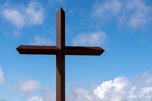 Steel cross against background of cloudy blue sky at Saint Anthony Greek Orthodox Monastery in Florence, Arizona.
