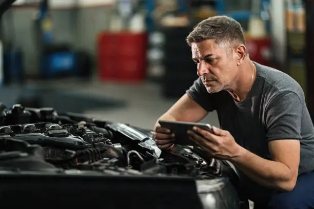 Car mechanic using digital tablet while repairing analyzing engine in auto repair shop.