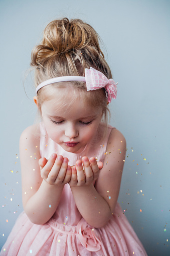 Portrait of cute 5 years old girl blowing gold glitter or pixie dust. Xmas, New Year, birthday or party time concept.