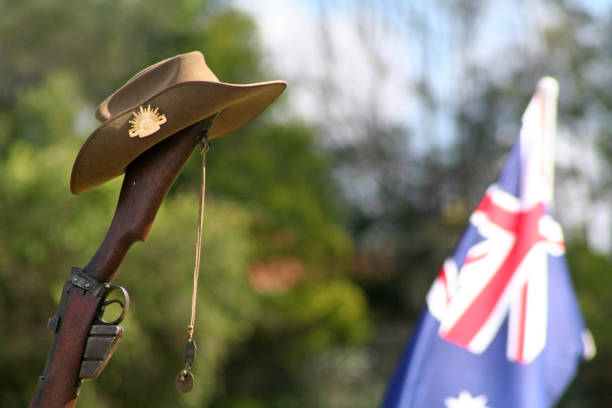 close-up of an upturned australian 303 rifle butt upon which sits a traditional australian slouch hat with rising sun badge, dogtags and the australian national flag on anzac day - bayonet imagens e fotografias de stock