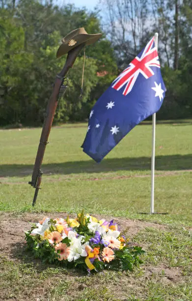 Vertical (portrait) shot of an upturned, vintage Australian Army 303 rifle and bayonet, a soldier's dogtags, iconic slouch hat, floral wreath and the Australian flag during an ANZAC Day remembrance service to honour all servicemen and women who have served, with emphasis on those who have been killed or injured in wars from the Sudan, Boer War, World War 1, World War 2, Korea, Vietnam, Iraq and Afghanistan or have served in peacekeeping missions. This image could be used to suit a range of themes and contexts relating to Australian military service or traditions.