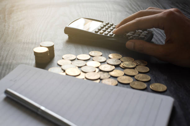 istock Close up hand of man using  calculator with gold coins, pen, notebook on black table 1191796048