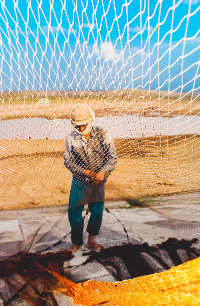Madiun, Indonesia - August 26, 2003: A fisherman sews a net near the dawuhan reservoir that dries the water in Madiun, East Java, Indonesia